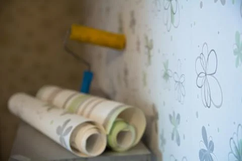 Two rolls of wallpaper and a roller lie against Stock Photos