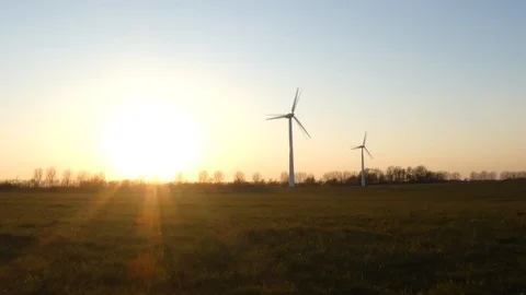 Two rotating wind turbines with setting sun on a wintry meadow - slow motion Stock Footage 106513523