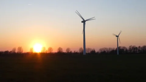 Two rotating wind turbines with setting sun on a wintry meadow - slow motion Stock Footage 106518443