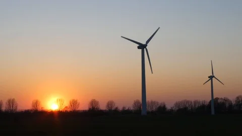 Two rotating wind turbines with setting sun on a wintry meadow Stock Footage 106533855