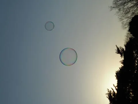 Two round bubbles floating away, lit by the setting sun. Stock Photos