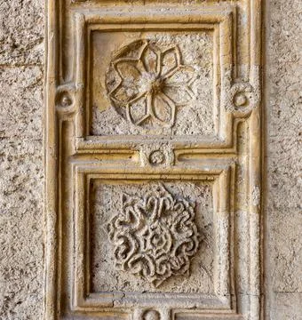 Two round floral patterns carved into ancient stone wall of Mamluk era mosque of Stock Photos