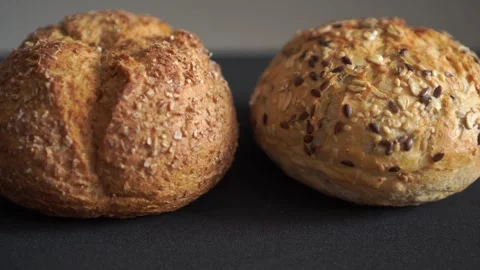 Two round multigrain bread rolls on dark surface studio loop video Video stock 318839506