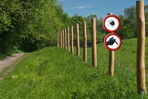 Two round red warning signs on a fence post in front of a green meadow. Bo... Stock-Fotos