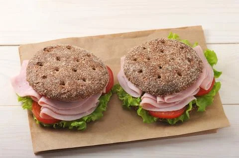 Two round sandwich of rye bread with ham, tomato and lettuce on paper Foto stock