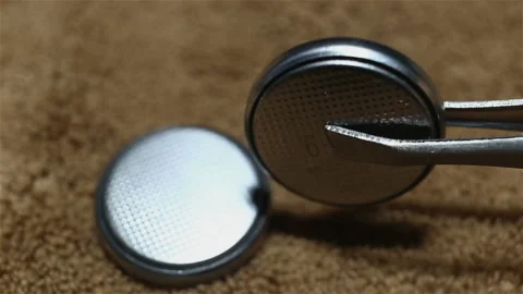 Two round silver batteries close-up, on a brown background, real time. One disch Stock Footage 149211423