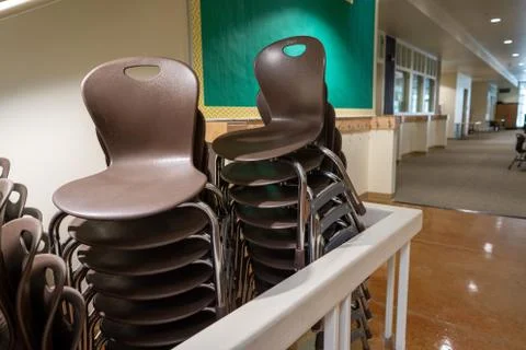 Two rows of brown stacking chairs at a school setting piled under stairs Stock Photos