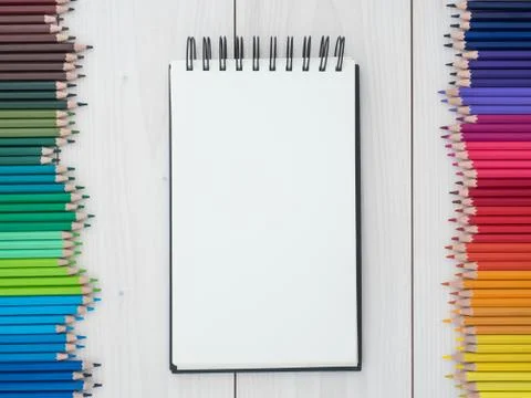 Two rows of colored pencils and notebook on wooden background Stock Photos