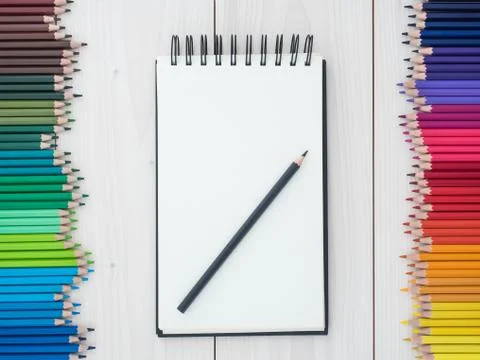 Two rows of colored pencils and notebook on wooden background Foto stock