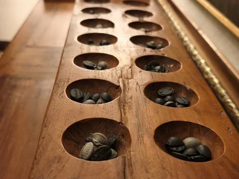 Two rows of congklak pits filled with dark playing seeds Stock Photos