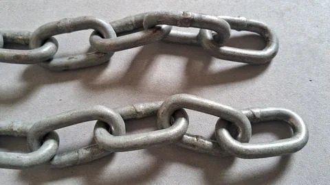 Two rows of heavy industrial metal chains on grey concrete Stock Photos