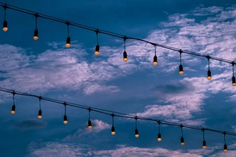 Two rows of warm white light bulbs turn on with the sky in the background. Stock Photos