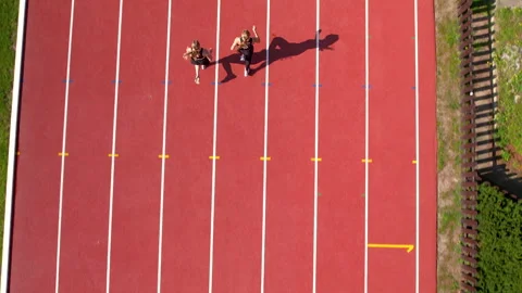Two runners mid-stride on parallel track lanes, shadow stretching, Stock-Footage 291076042
