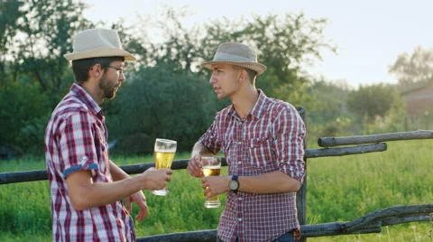 Two rural Man in hats drinking beer at a wooden fence. In the countryside Stock Footage 65454272
