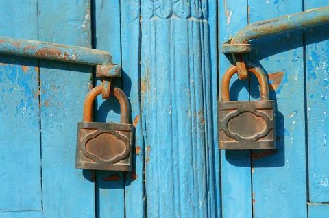 Two rusted padlocks fastened to worn blue double doors Stock Photos