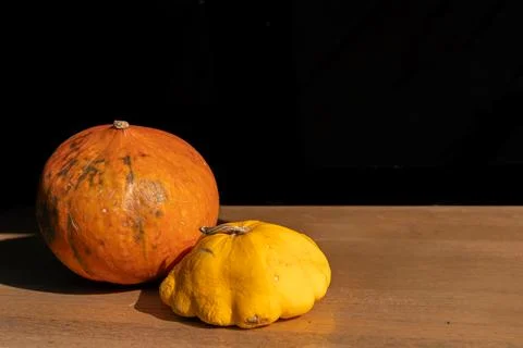 Two rustic pumpkins resting on a wooden table against a dark background in Foto stock