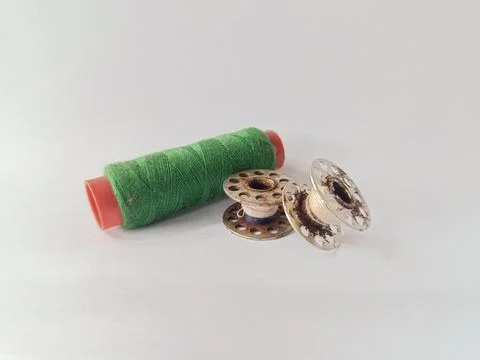 Two rusty sewing machine bobbins and a spool of green thread. White background. Stock Photos