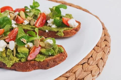 Two rye bread toasts with mashed avocado, tomatoes and feta cheese. Stock Photos