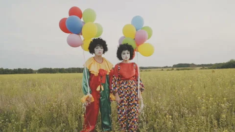 Two sad clowns with balloons stand in the field. Stock Footage 92182902