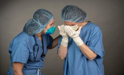 Two sad nurses one with old, broken mask consoling each other outside the OR. Stock Photos