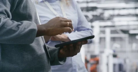 Two Safety Supervisors Coordinating Tasks in Bright, Modern Manufacturing Plant Stock-Footage 325731265