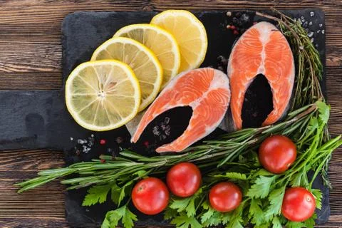 Two salmon steakes with greenery, lemon and cherry tomatoes on the black boar Stock Photos