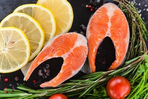 Two salmon steakes with greenery, lemon and cherry tomatoes on the black boar Stock Photos