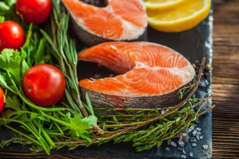 Two salmon steakes with greenery, lemon and cherry tomatoes on the black boar Stock Photos