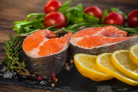 Two salmon steakes with greenery, lemon and cherry tomatoes on the black boar Stock Photos