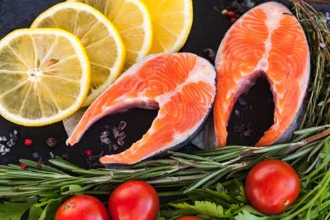 Two salmon steakes with greenery, lemon and cherry tomatoes on the black boar Stock Photos
