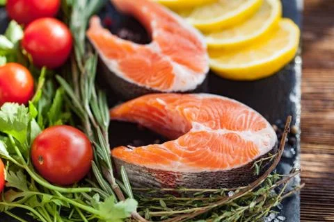 Two salmon steakes with greenery, lemon and cherry tomatoes on the black boar Stock Photos