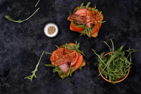 Two sandwiches with aragula, fried ham, tomatoes on dark background, top view. Foto stock