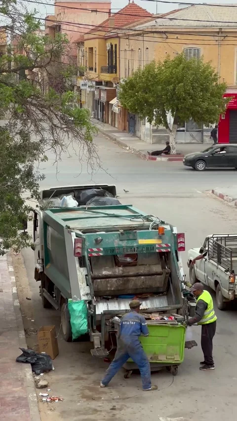 Two sanitation workers load garbage into a green waste truck on a city street du Stock Footage 314394959