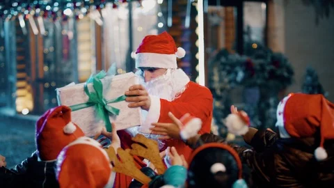 Two Santa clauses helping each other to give gifts to group, queue of children . Stock Footage 120573420