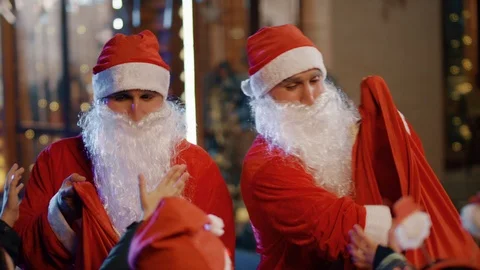 Two Santa clauses helping each other to give gifts to group, queue of children . Stock Footage 120573576