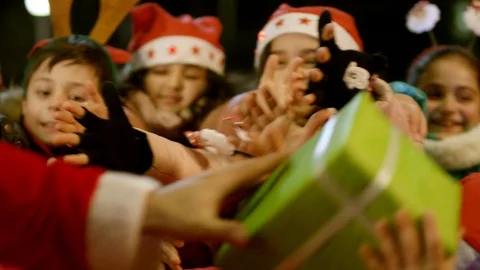 Two Santa clauses helping each other to give gifts to group, queue of children . Stock Footage 120573869
