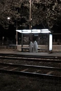 Two scary ghosts sitting at a train tram stop eerily 스톡 사진