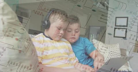 Two school-age boys sitting on sofa at home, sharing laptop with headphones and Stock Photos