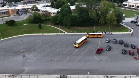 Two school buses arrive at circular parking lot as students wait along curved Stock Footage 345727846
