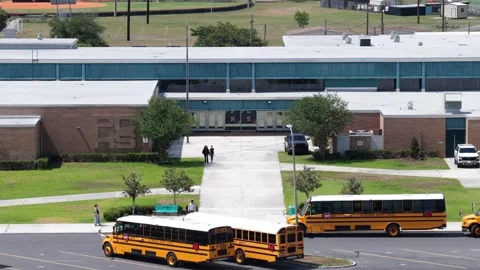 Two school buses idle with stop arms extended outside brick high school Video stock 340863740
