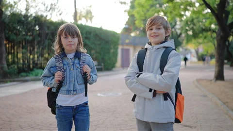 Two school kids with backpacks standing in park pathway smiling at camera. Stock Footage 338139519