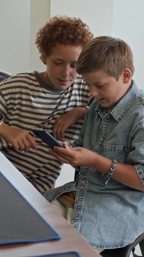 Two Schoolboys Looking through Online Shorts in Smartphone and Laughing Stock Footage 316483819