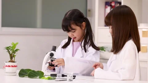 Two Schoolgirls in Lab Coats Learning Biology with Microscope Stock Footage 346017999