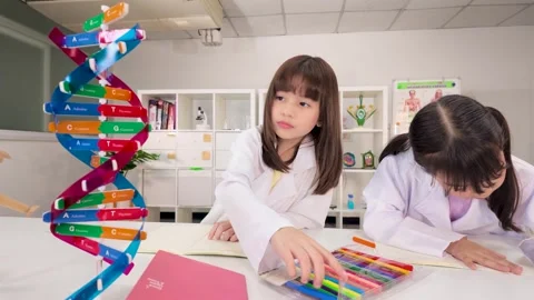Two Schoolgirls in Lab Coats Studying Genetics Beside DNA Model 库存影片 346365325