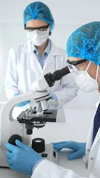 Two scientists in blue protective hairnets, masks and glasses conduct research Stock Photos
