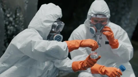 Two scientists in full hazmat suits examine a liquid sample 스톡 동영상 346120275