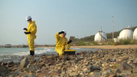 Two scientists in yellow suits are collecting water samples from the shore Vídeos de archivo 340085498