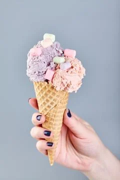 Two scoops of ice cream in waffle cone in female hand on gray background Stock Photos