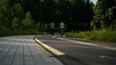 Two scooters are riding along a bike path next to the forest Stock Photos