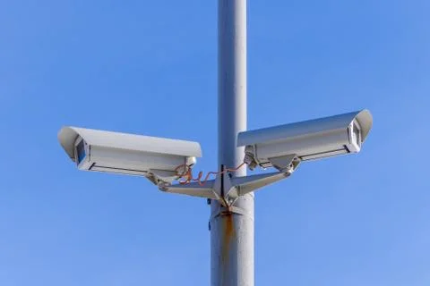 Two security cameras against the blue sky are monitoring. Stock Photos